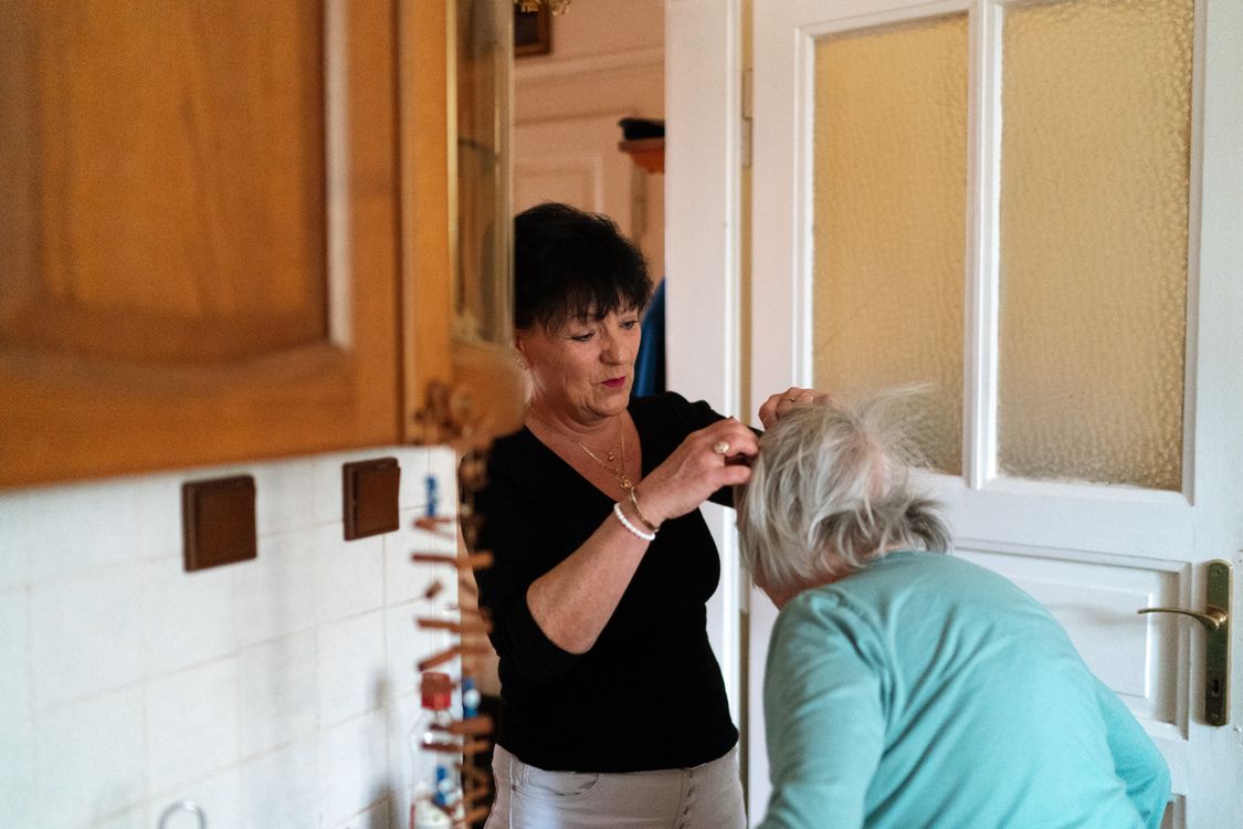 A home care aide helping an older woman stand up in a bright living room